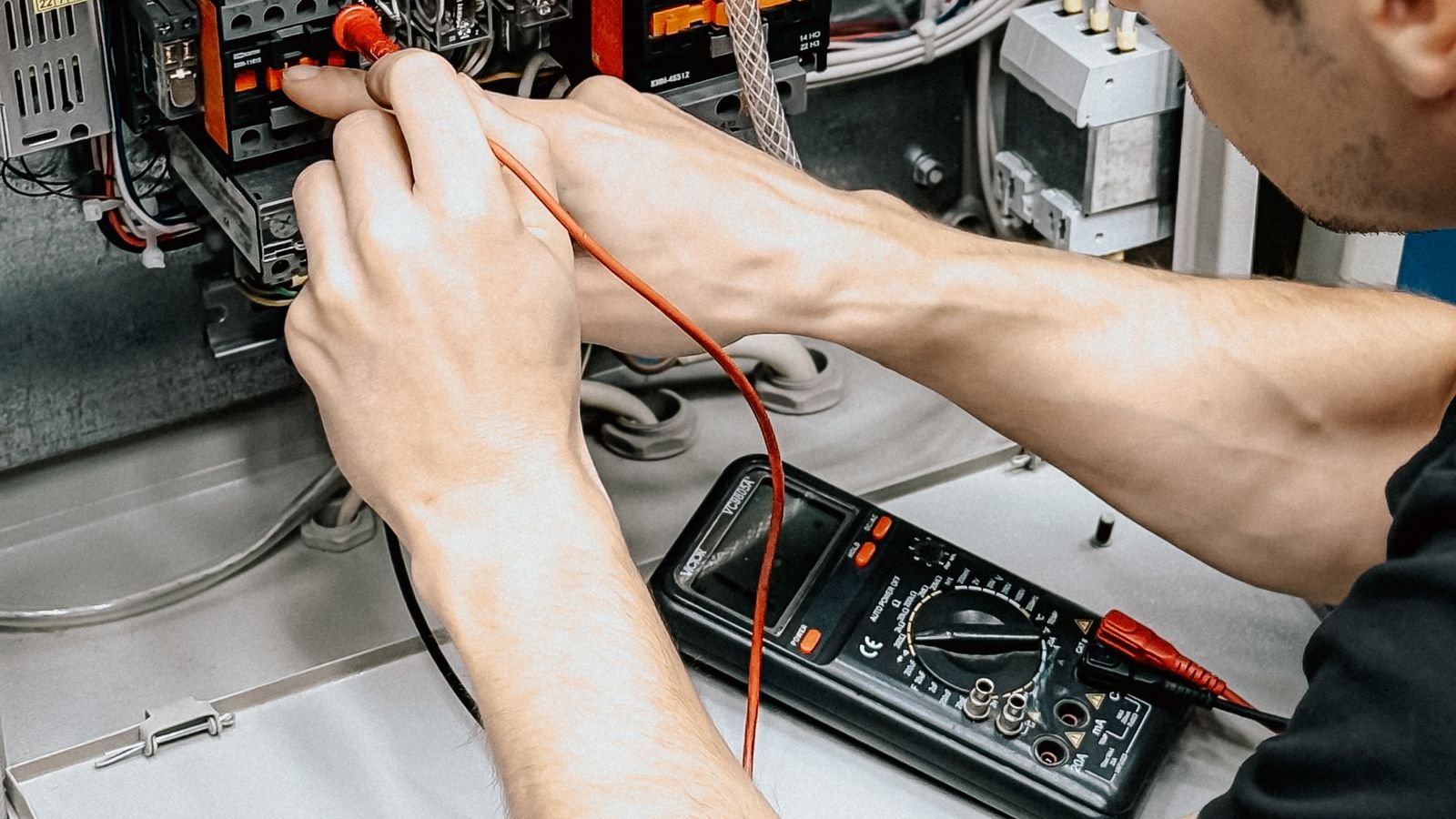 Electrician testing an industrial electrical panel with a multimeter during Titania output fault commissioning